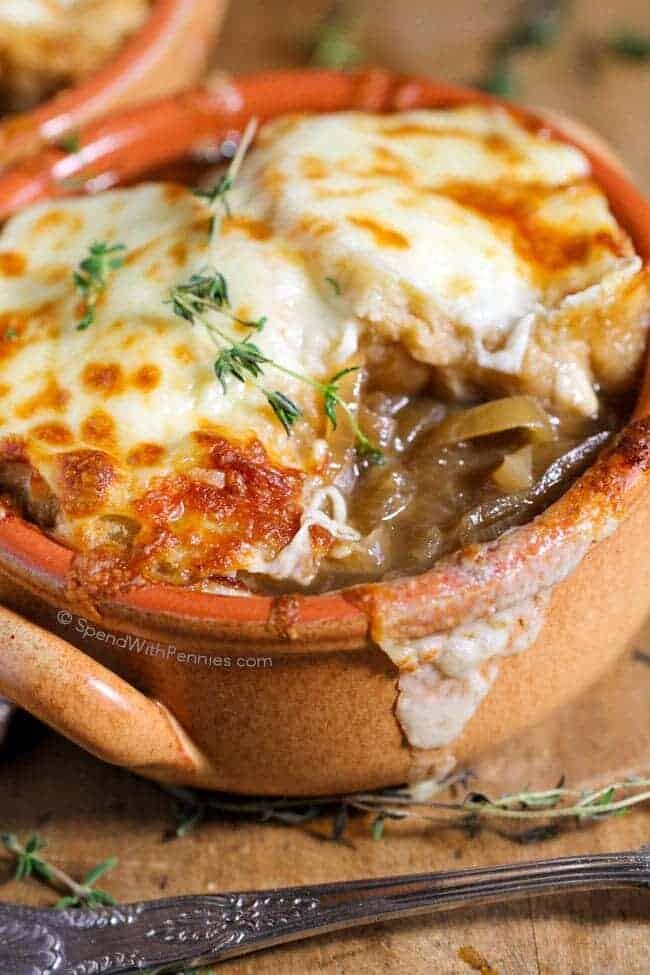 closeup of a bowl of French onion soup with cheese and thyme garnish with a bite out of it