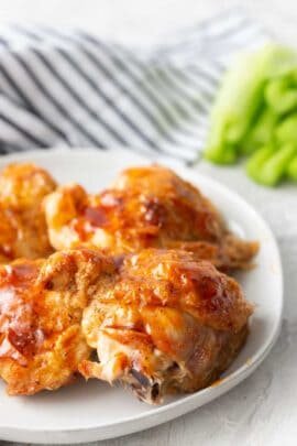 4 pieces of air fries chicken thighs, skin on, with BBQ sauce brushed over the top, celery in the background