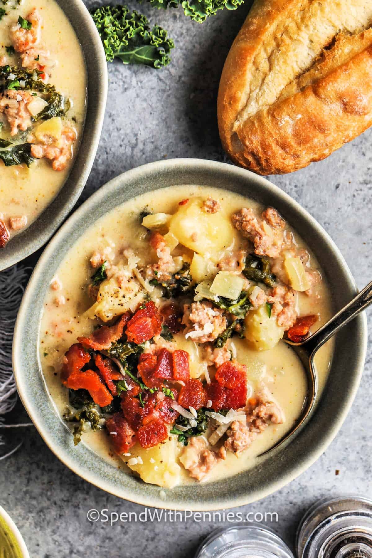 a bowl of zuppa toscana topped with bacon next to a baguette