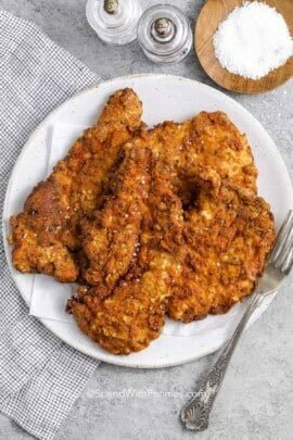 Crispy fried chicken breast on a plate next to salt